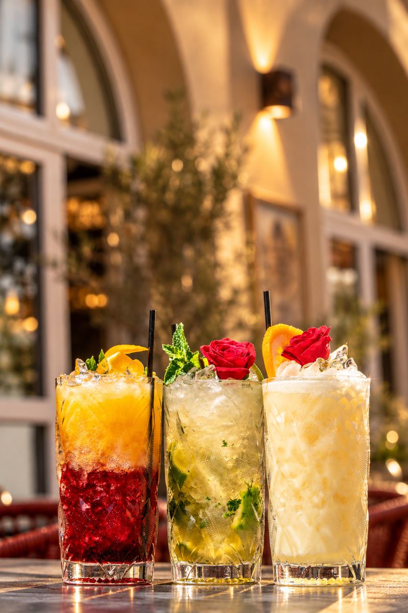 Drei Cocktails mit Rosen vor den Bogenfenstern des Eingangs